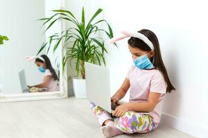 Little caucasian girl with bunny ears and medical mask on her face on a white background. Easter concept. Coronavirus protected photo