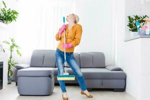Young woman with housecleaning gear dances in the living room. photo