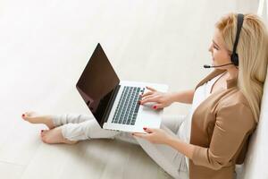 Focused attentive woman in headphones sits with laptop, looks at screen, makes notes, learns foreign language in internet, online study course, self-education on web, consults client by video photo