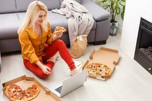 comercio electrónico mujer. joven hembra utilizando computadora para en línea compras, sentado en el piso y comiendo Pizza. foto