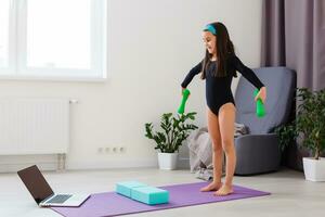Little girl doing yoga exercise in fitness studio with big windows on background photo