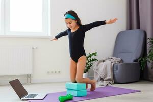 Little girl doing yoga exercise in fitness studio with big windows on background photo