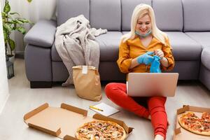 woman in protective gloves and mask with pizza at home during quarantine. service food order online delivery in quarantine covid-19. airline food. photo