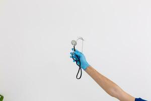 Caucasian male hand, wearing medical gloves, holding a stethoscope, white background photo