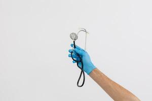 Caucasian male hand, wearing medical gloves, holding a stethoscope, white background photo