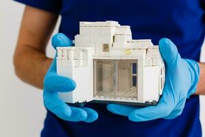 small wooden house in the palm of your hand with a white medical rubber glove, blue background, wooden model of the house, quarantine concept, coronavirus pandemic, medicine during an epidemic photo