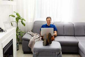 Happy young man in t-shirt sitting at home, working on laptop computer, smiling. photo