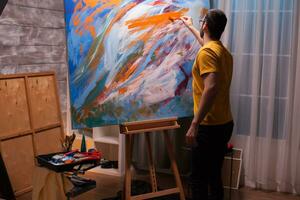 Young man with painting skill working on large canvas in art studio. Modern artwork paint on canvas, creative, contemporary and successful fine art artist drawing masterpiece photo