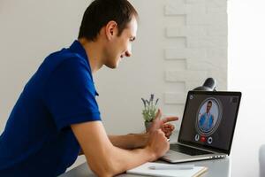 Man having video chat with doctor on laptop at home photo