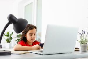Remote lessons. The child smiles happily and gets knowledge remotely. Little girl study online learning from home with laptop. Online school. photo