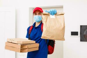 Delivery man employee in red cap t-shirt uniform mask gloves give food order pizza boxes isolated on yellow background studio. Service quarantine pandemic coronavirus virus flu 2019-ncov concept photo