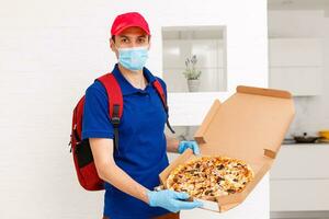 entrega hombre empleado en rojo gorra camiseta uniforme máscara guantes dar comida orden Pizza cajas aislado en amarillo antecedentes estudio. Servicio cuarentena pandemia coronavirus virus gripe 2019-ncov concepto foto