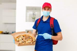 entrega hombre empleado en rojo gorra camiseta uniforme máscara guantes dar comida orden Pizza cajas aislado en amarillo antecedentes estudio. Servicio cuarentena pandemia coronavirus virus gripe 2019-ncov concepto foto