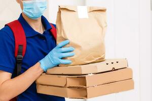 Delivery man employee in red cap t-shirt uniform mask gloves give food order pizza boxes isolated on yellow background studio. Service quarantine pandemic coronavirus virus flu 2019-ncov concept photo