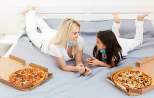 mother and daughter lie in bed at home with pizza during quarantine, quarantine leisure photo
