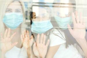 Family, standing behind the window, at home, quarantine due to coronavirus photo