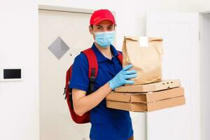 entrega hombre empleado en rojo gorra camiseta uniforme máscara guantes dar comida orden Pizza cajas aislado en amarillo antecedentes estudio. Servicio cuarentena pandemia coronavirus virus gripe 2019-ncov concepto foto