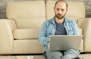Adult man using laptop sitting on living room carpet. photo