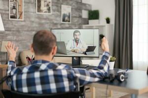 Patient on video call with doctor talking about his rehabilitation. Young immobilized guy sitting at home in front of laptop, talking with his doctor about the process of rehabilitation on video call. photo