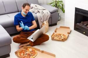 Man in protective gloves and mask using laptop for online food order during quarantine, closeup. Delivery service photo