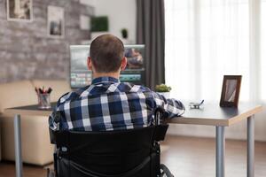 Video editor in wheelchair working on film post production. Invalid videographer doing his business online, using high technology, sitting in his apartment, working remotely in special conditions. photo