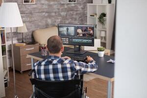 Video editor working from home sitting in wheelchair infront the computer. Invalid videographer doing his business online, using high technology, sitting in his apartment, working remotely in special conditions. photo