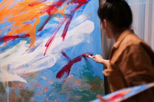 Young artist in art workshop using red paint on large canvas to create a contemporary painting. Modern artwork paint on canvas, creative, contemporary and successful fine art artist drawing masterpiece photo