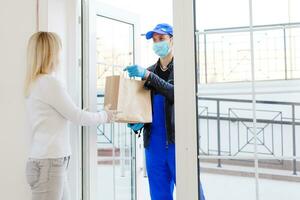 Courier in protective mask delivers parcel, customer in medical gloves receives box. Delivery service under quarantine, disease outbreak, coronavirus covid-19 pandemic conditions. photo