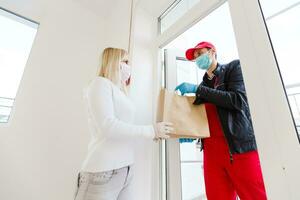 Coronavirus. Woman wearing a medical mask and rubber gloves receiving a package from a delivery man indoors. Virus prevention and protocols. Stay at home. Delivery service. Disinfecting the package. photo