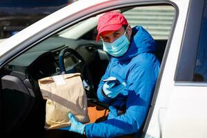 Courier in protective mask and medical gloves delivers takeaway food. Delivery service under quarantine, disease outbreak, coronavirus covid-19 pandemic conditions. photo