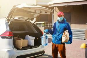 Courier in protective mask and medical gloves delivers takeaway food. Delivery service under quarantine, disease outbreak, coronavirus covid-19 pandemic conditions. photo