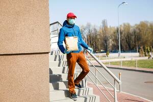 Delivery man holding paper bag with food, food delivery man in protective mask photo