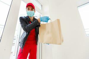 delivery man in protective mask and medical gloves holding a paper box. Delivery service under quarantine, disease outbreak, coronavirus covid-19 pandemic conditions. photo