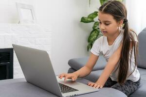 aburrido pequeño niña con ordenador portátil a hogar. linda niño haciendo deberes en computadora. moderno en línea educación, comunicación y tecnología concepto, Copiar espacio. foto