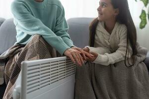 Family warming hands near electric heater at home, closeup photo