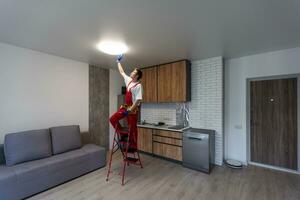 Worker installing lamp on stretch ceiling indoors. photo