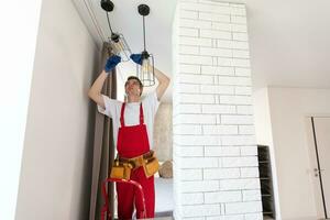 Worker installing lamp on stretch ceiling indoors. photo