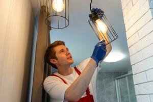 Electrician at work. Service for the repair of electrical wiring and replacement of ceiling lamps. A builder is installing a loftstyle wooden ceiling. Rentagent helps with the housework photo