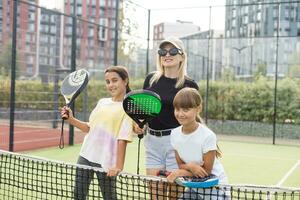 Cheerful coach teaching child to play tennis while both standing on tennis court photo