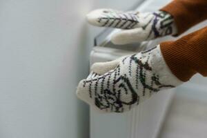 Closeup of woman warming her hands on the heater at home during cold winter days, top view. Female getting warm up her arms over radiator. Concept of heating season, cold weather. photo