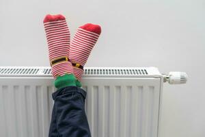 Children's feet in warm socks on a radiator. Girl warming up in a cold apartment photo