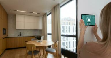 Controlling home with a digital touch screen panel installed on the wall in the living room. Concept of a smart home and mobile application for managing smart devices at home. photo