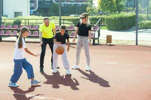 verano vacaciones, deporte y personas concepto contento familia con pelota jugando en baloncesto patio de recreo foto