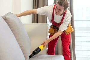 Handsome young man cleaning furniture. Process of deep furniture cleaning, removing dirt from sofa. Washing concept photo