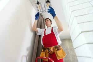 Electrician at work. Service for the repair of electrical wiring and replacement of ceiling lamps. A builder is installing a loftstyle wooden ceiling. Rentagent helps with the housework photo