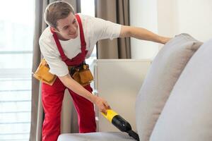 Rear View Of Young Male Worker Cleaning Sofa With Vacuum Cleaner photo