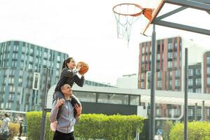 Father and teenage daughter playing basketball outside at court photo