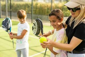 Cheerful coach teaching child to play tennis while both standing on tennis court photo