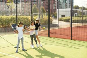 Cheerful coach teaching child to play tennis while both standing on tennis court photo