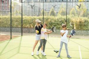 Young sporty woman with children playing padel game in court on sunny day photo